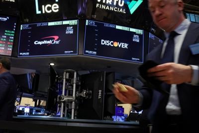 Screens display the logos and trading information for Capital One Financial and  Discover Financial as traders work on the floor at the NYSE in New York